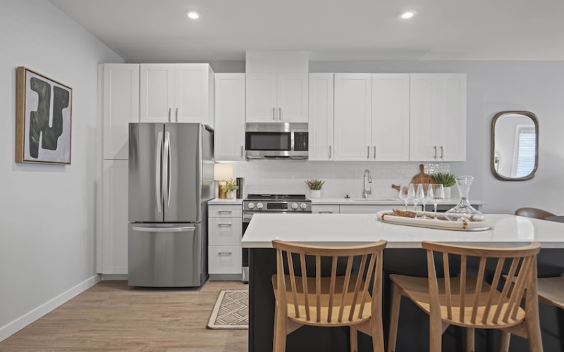 A kitchen with an island, chairs, white cabinetry, and stainless appliances 